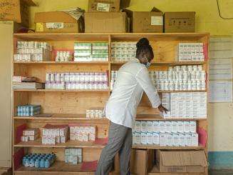 An MSF clinician in white coat picking ARVs out of boxes for a patient.