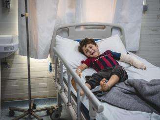 A smiling boy with an arm cast on a hospital bed in Mosul, Iraq.