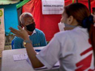 A patient sits at a table in front of an MSF staff member for a free X-ray at an MSF tuberculosis (TB) screening sites in Manila.