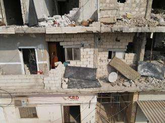 A gray concrete building that was damaged by the earthquake with windows blown in and crumbled balconies.