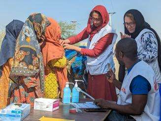 A group of MSF medics are clustered together outside in Dadu district, Pakistan, caring for women and their children.
