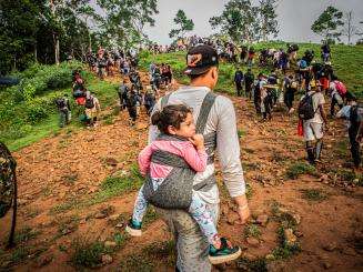 A migrant carries a child in a backpack as he crosses the Darién jungle between Colombia and Panama.