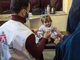 A small child is checked by an MSF staff member with her mother standing beside her in Afghanistan.