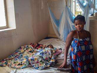 Woman standing next to her newborn twins resting on a hospital bed. 