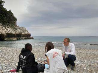 A man sits on the shores of Greece and is tended to by two MSF workers. 